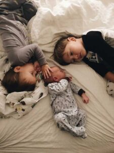 Empathic boy comforting infant brother on bed beside sibling